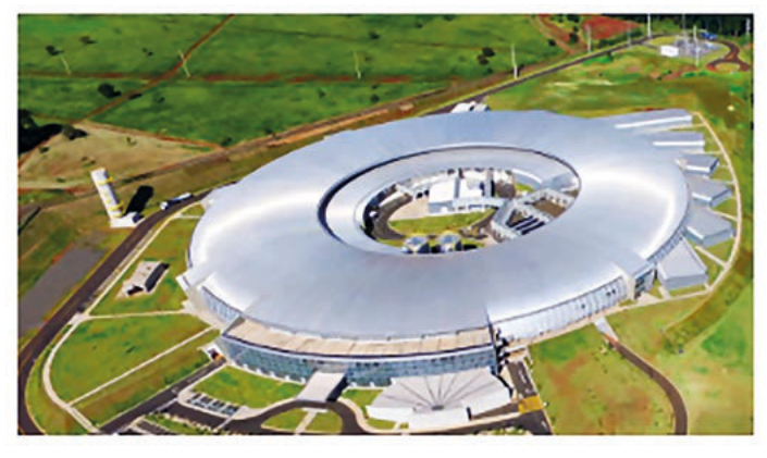 Fotografia aérea de um grande edifício circular com cobertura metálica, cercado por áreas verdes.
