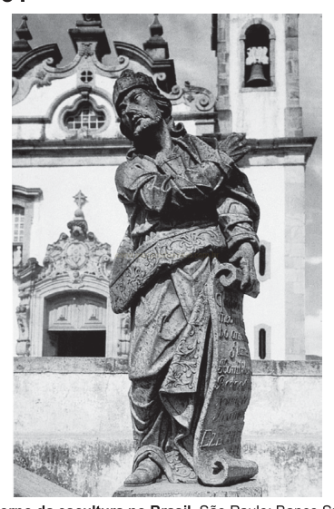 Fotografia em preto e branco de uma estátua de pedra de um homem em traje colonial diante de uma igreja.