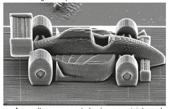 Micrografia em tons de cinza de um pequeno carro de corrida de brinquedo feito por impressão 3D, com estrias de camadas visíveis.