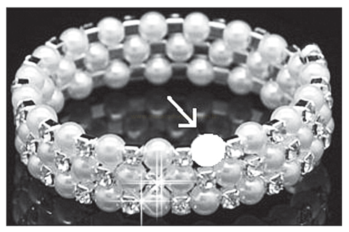 Bracelete de esferas claras e peças metálicas, visto em preto e branco, com uma seta apontando para uma esfera destacada.
