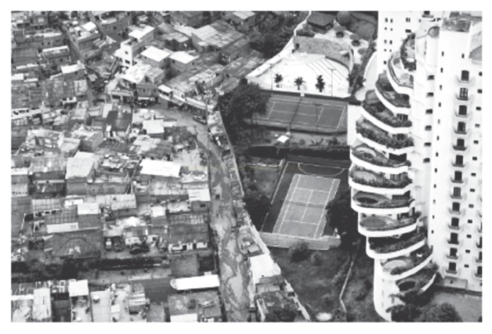 Fotografia aérea em preto e branco contrastando casas adensadas, quadras de tênis e um edifício alto com varandas curvas.