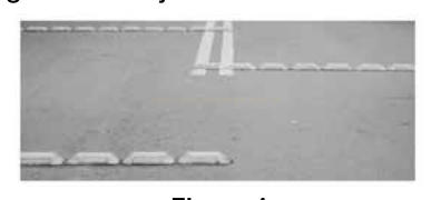 Fotografia em preto e branco de marcas brancas tracejadas na sinalização de um trecho de asfalto.