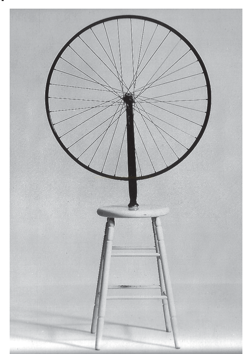 Fotografia em preto e branco de uma roda de bicicleta montada de cabeça para baixo sobre um banquinho branco.
