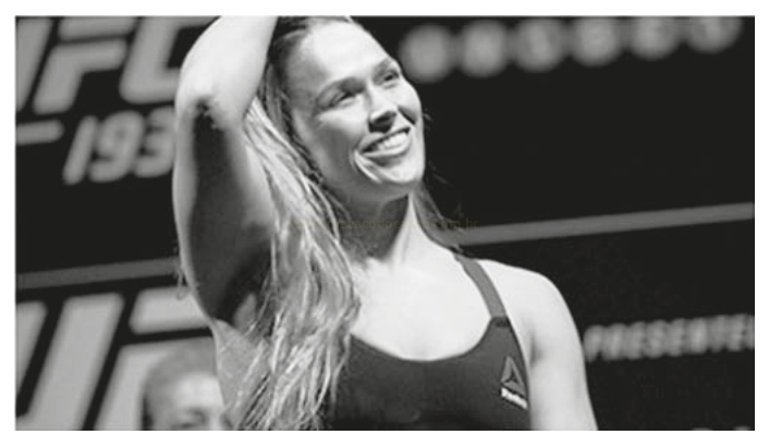 Fotografia em preto e branco de uma atleta sorrindo e levantando o braço.