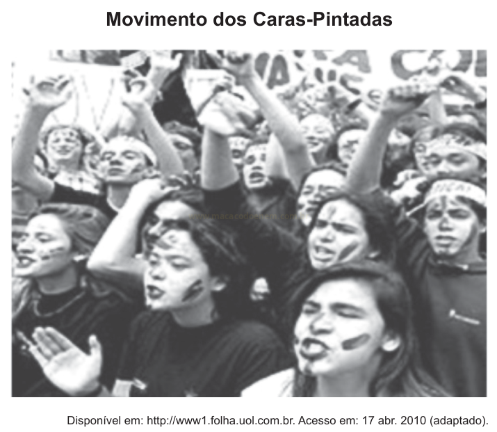 Fotografia em preto e branco de uma multidão de jovens com os rostos pintados e braços levantados.