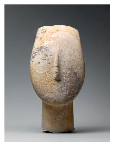 Fotografia de uma pequena escultura em pedra que lembra uma cabeça com nariz em relevo.