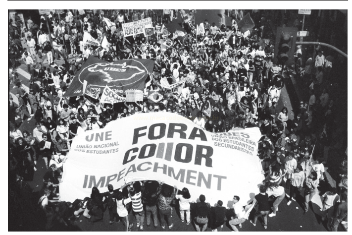 Fotografia aérea em preto e branco de multidão em manifestação segurando uma grande faixa com dizeres de impeachment.